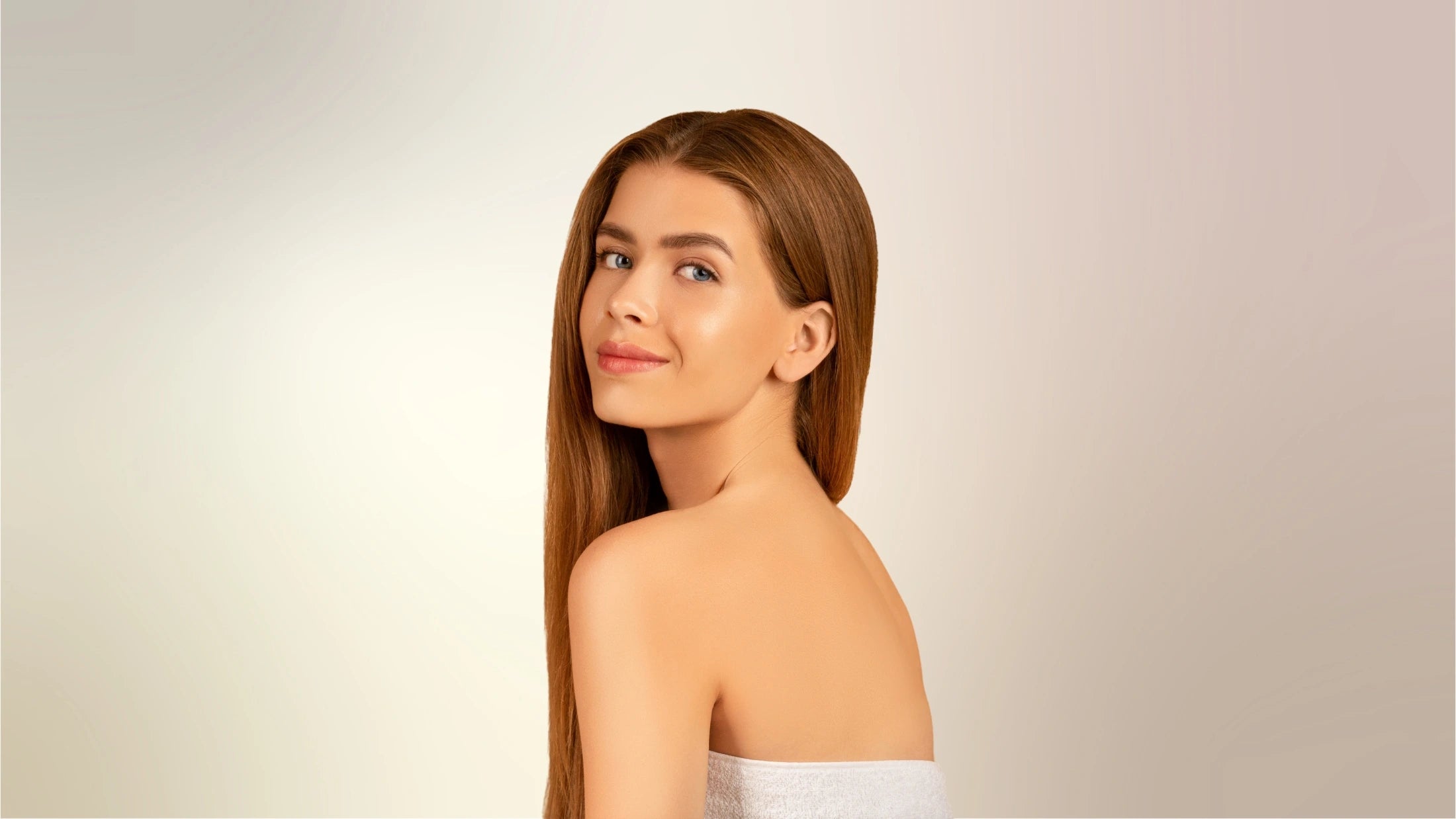 Woman with long brown hair wearing a white strapless top on a beige background